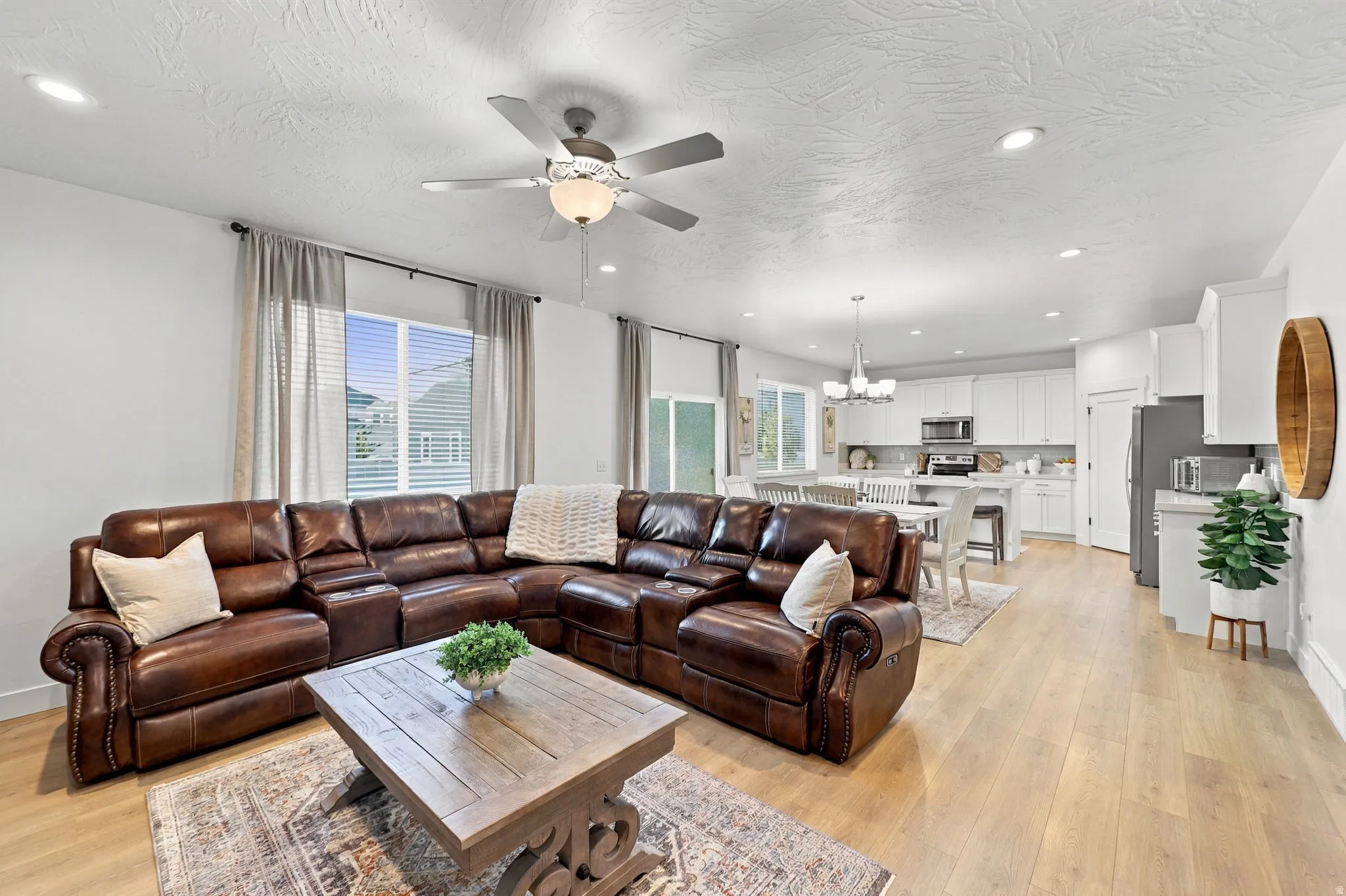 Recessed lighting, wood-finish flooring, ceiling fan with integrated lighting, white upper and lower cabinetry, and stainless steel appliances