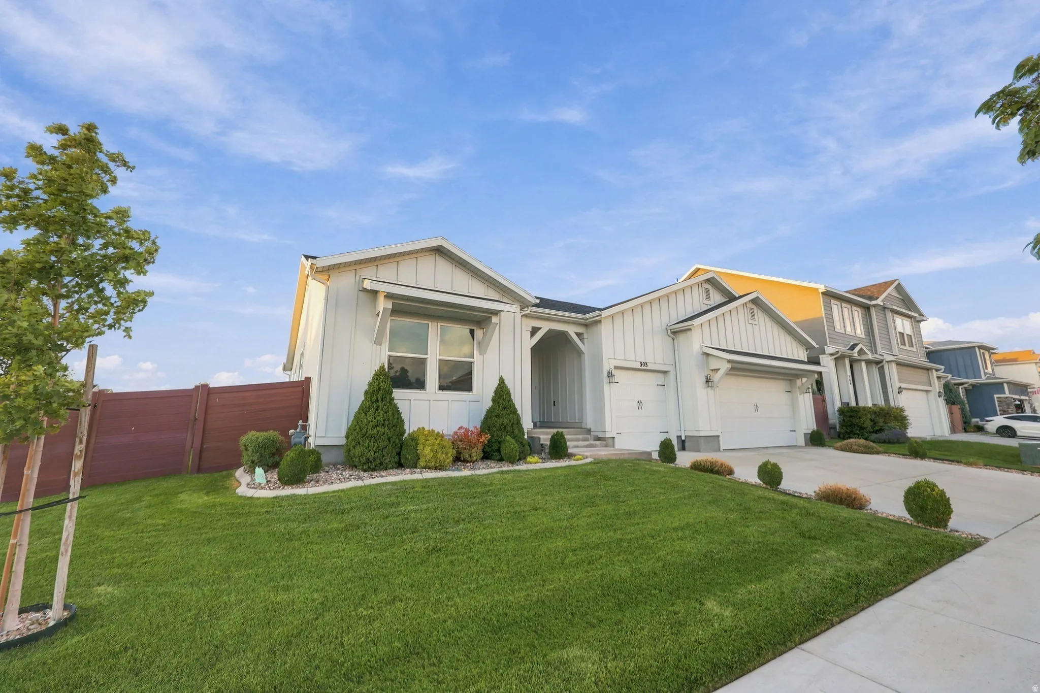 Contemporary-style exterior with white vertical siding, dual garage doors, a covered entry, and a manicured front lawn