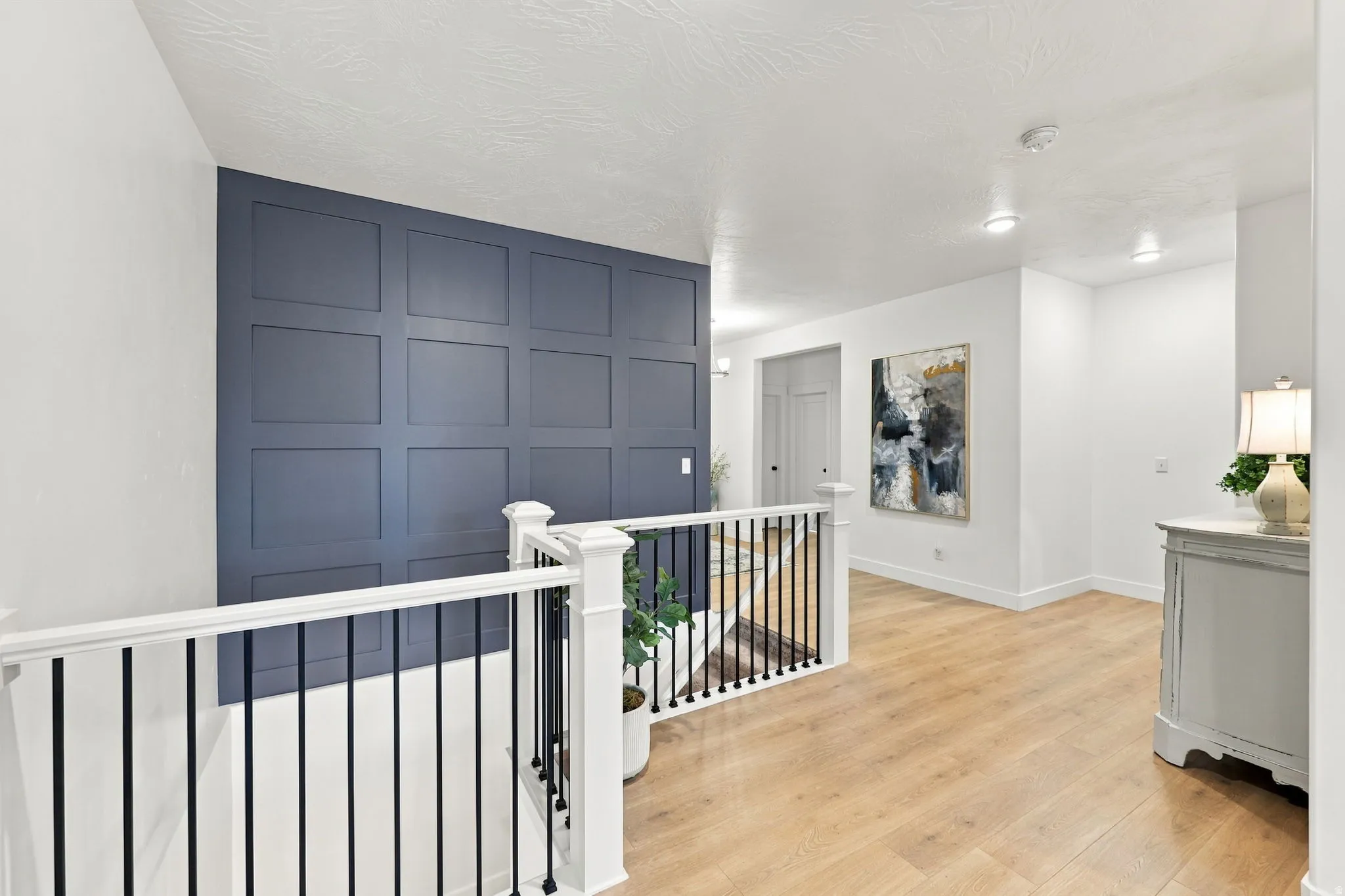 Wood-finish flooring, white walls, recessed lighting, and a decorative paneled accent wall with white trim
