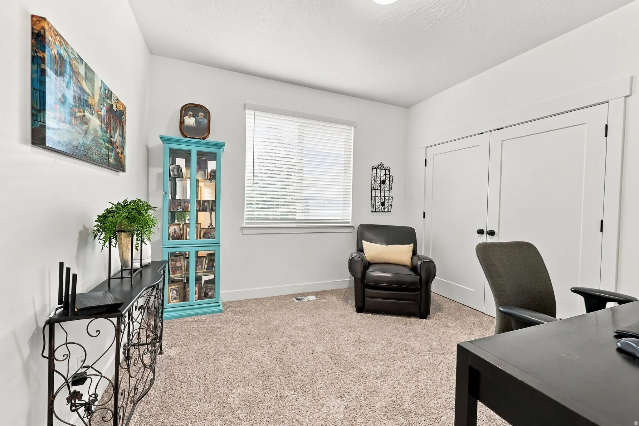 Plush carpet flooring, white painted walls, and a window with blinds provide natural light