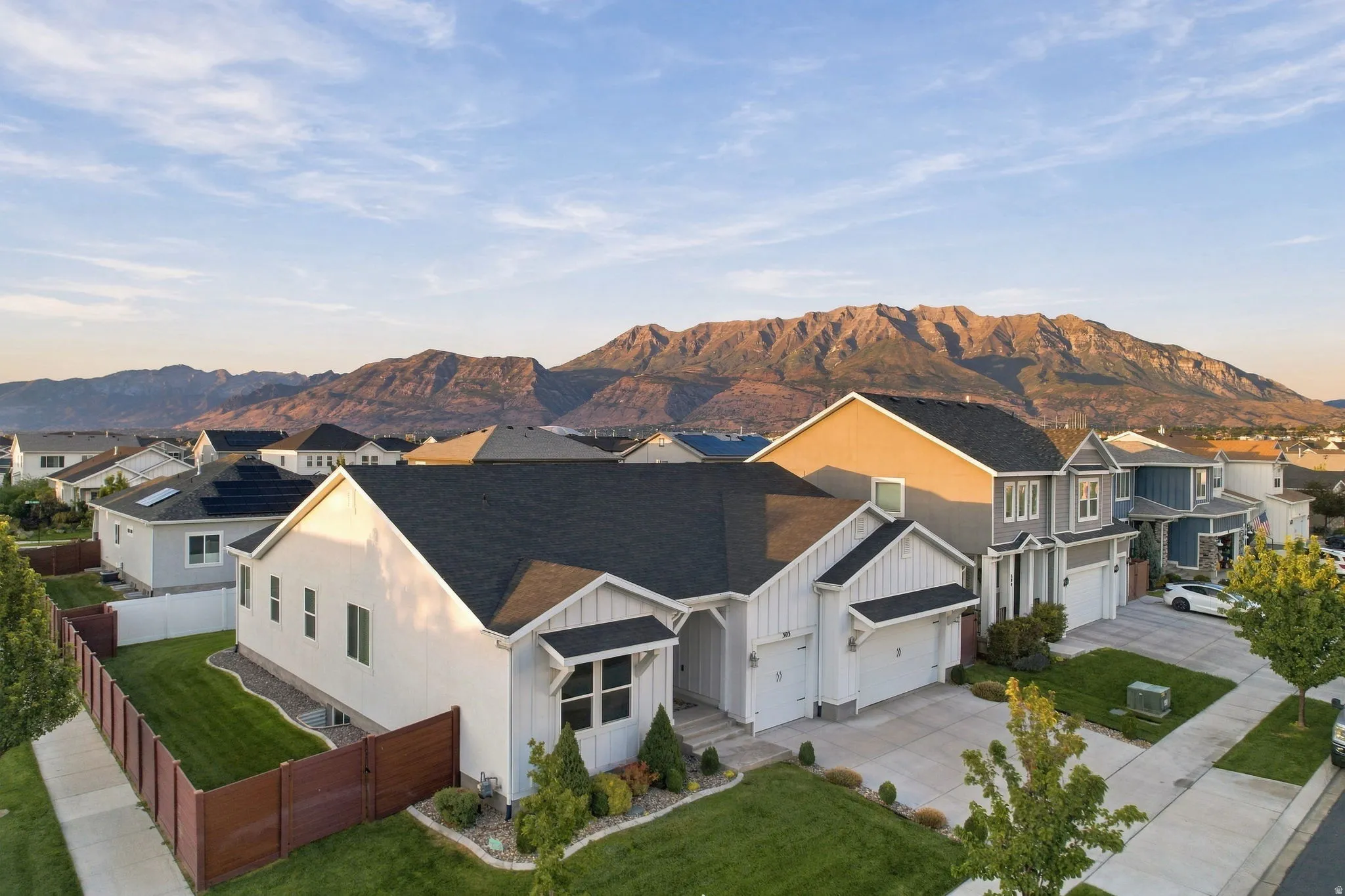 Contemporary exterior with white siding and dark trim, two-car garage, manicured front lawn, and mature landscaping