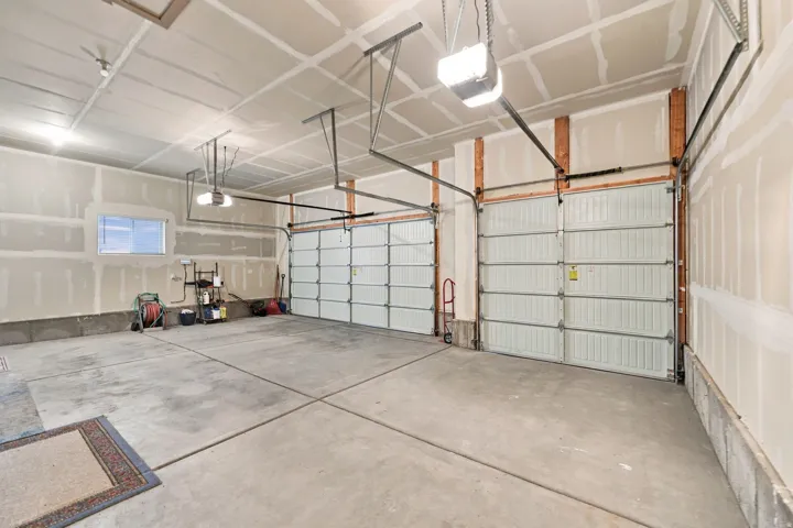 Two white garage doors with automatic openers, a concrete floor, and overhead lighting