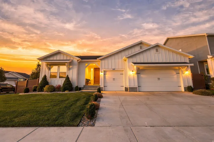 White board and batten exterior with a gabled roofline, integrated two-car garage, concrete driveway, and front lawn landscaping