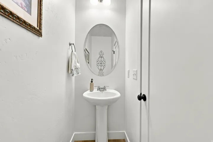 Pedestal sink with chrome faucet, oval mirror, and wall-mounted light fixture