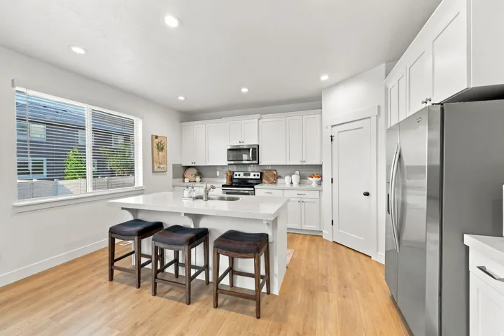 Bright kitchen featuring white cabinetry, stainless steel appliances, a center island with countertop seating, wood-finish flooring, and recessed lighting
