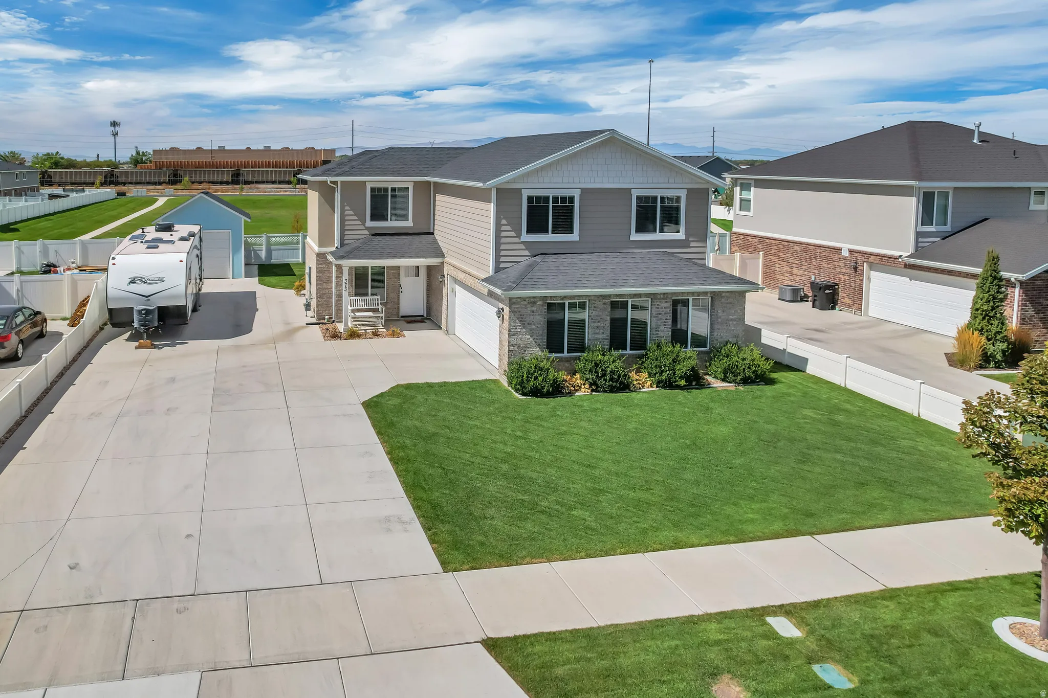 Two-story residence featuring a gray exterior with stone accents, a two-car garage, and a lush green lawn