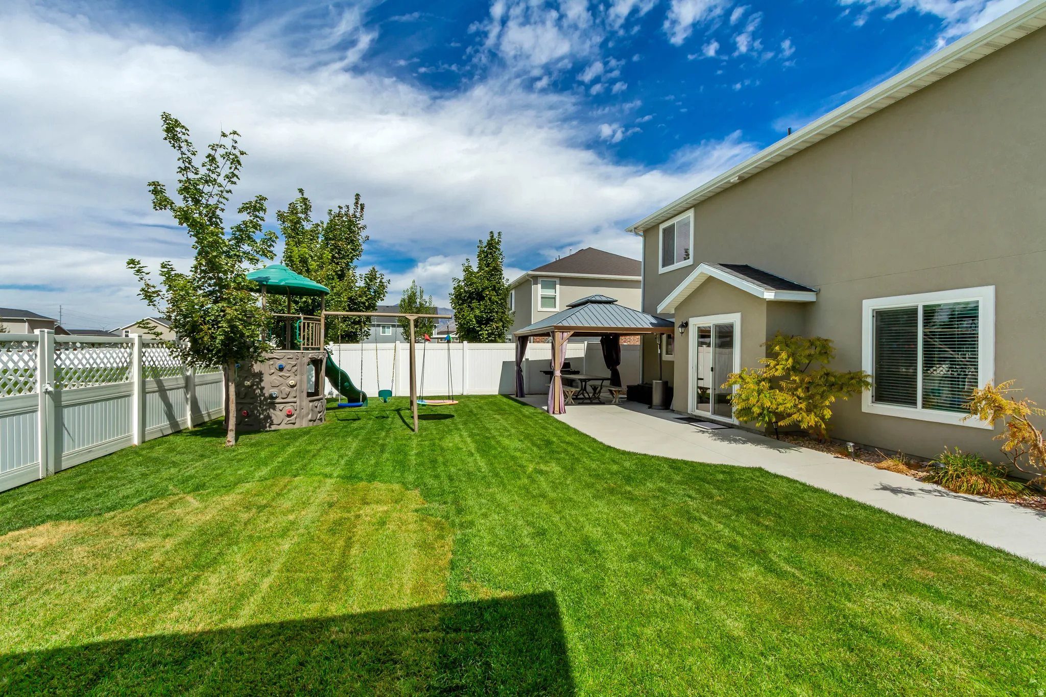 Expansive green lawn, white privacy fencing, paved patio area, and outdoor gazebo structure