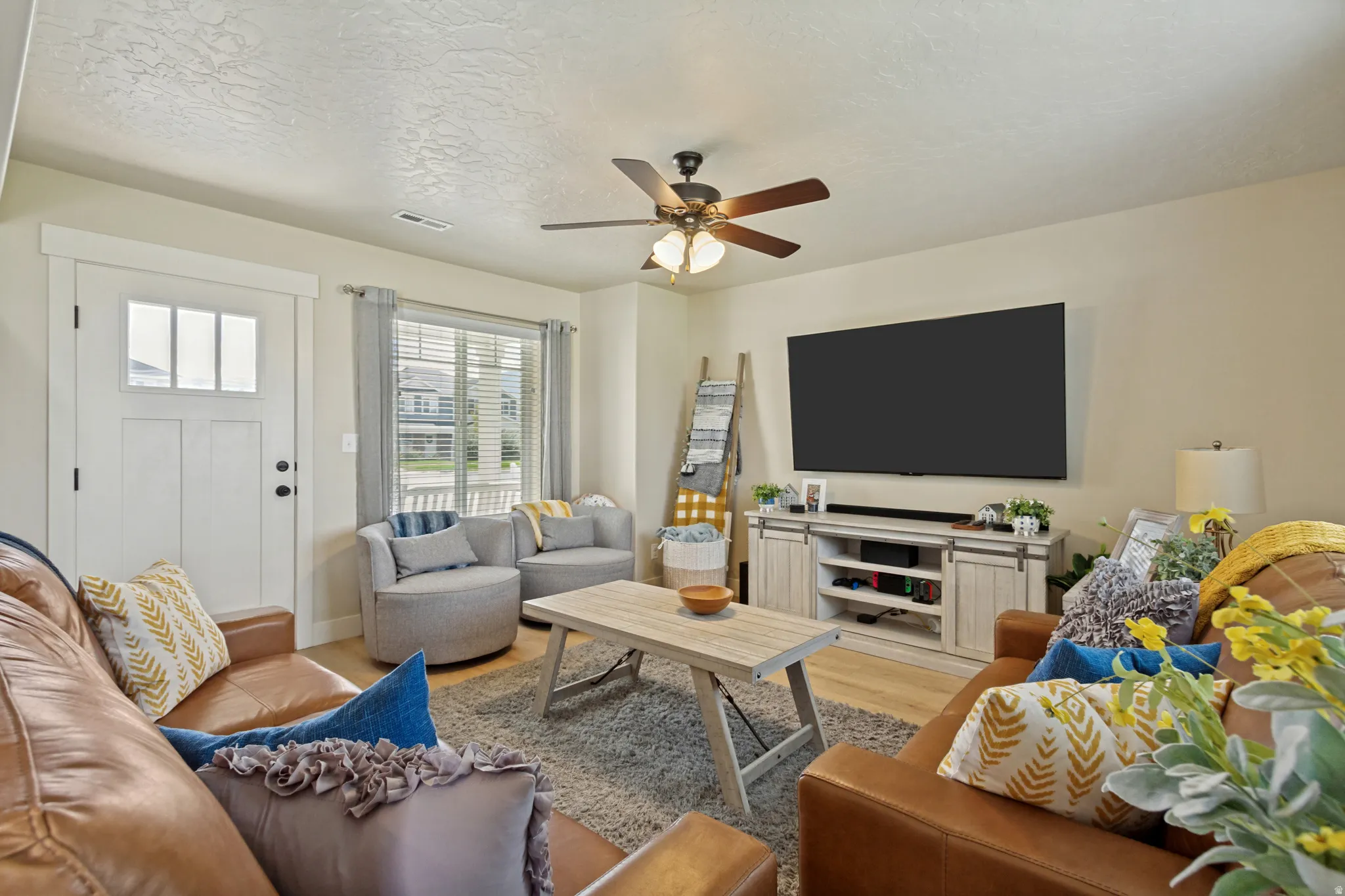 Living area featuring wood-finish flooring, a ceiling fan, and a transom window door with sidelights