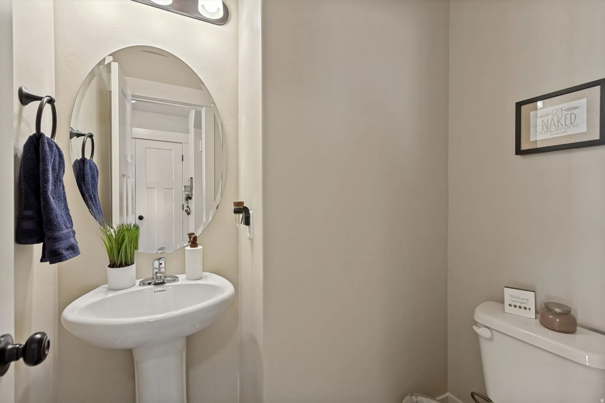 Pedestal sink with chrome fixtures, oval mirror, and wall-mounted light fixture