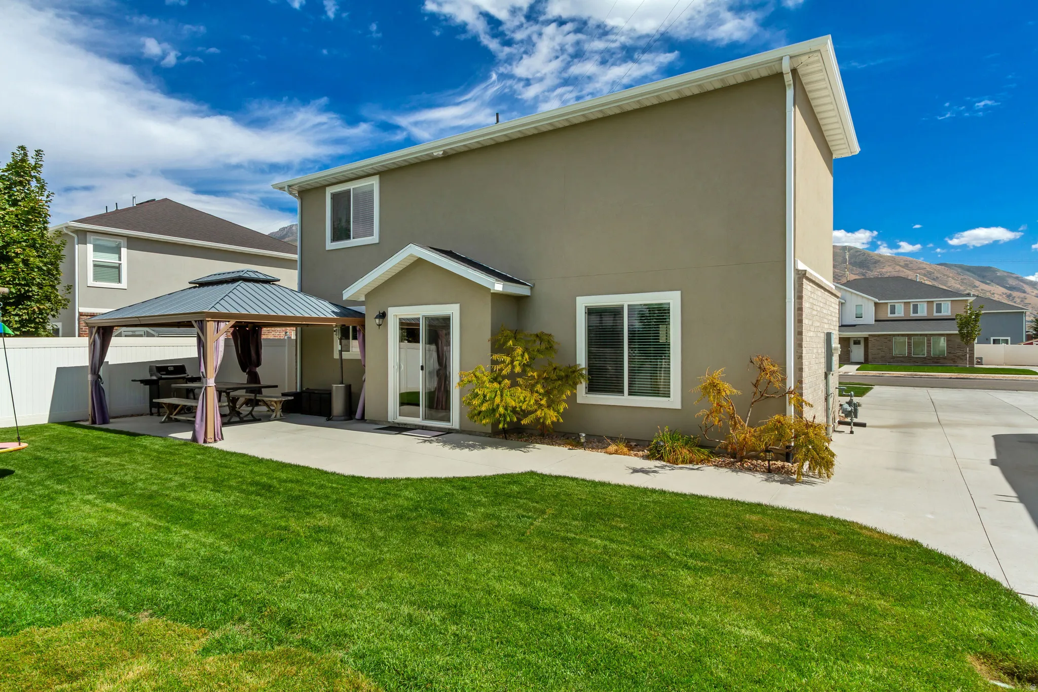 Expansive backyard featuring a manicured lawn, concrete patio, and white privacy fencing
