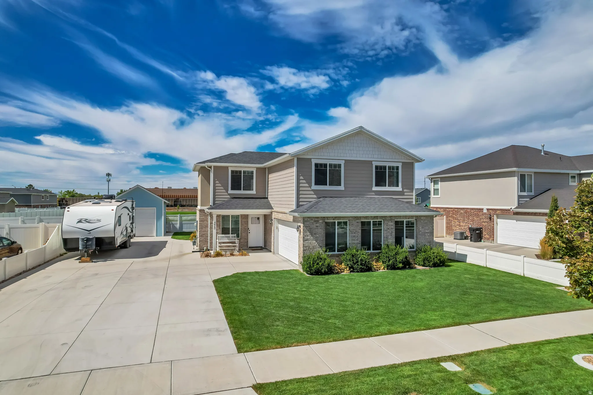Two-story residence featuring a gray siding and brick facade, an attached two-car garage, and a detached shed