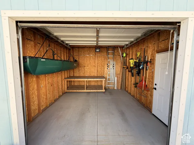 Shed/Workshop with exposed wood-paneled walls and a concrete floor. 15' +- feet deep. 13' +- wide. Manually operated overhead door.