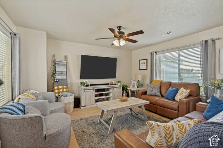Living room with recessed can lighting, laminate flooring, ceiling fan with integrated lighting, and multiple windows with blinds