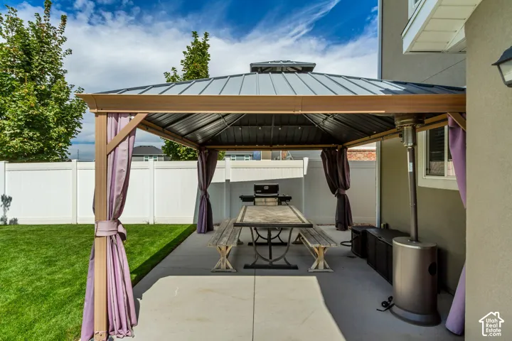 Expansive concrete patio featuring a metal-roofed gazebo, privacy curtains, and a manicured lawn enclosed by a white privacy fence