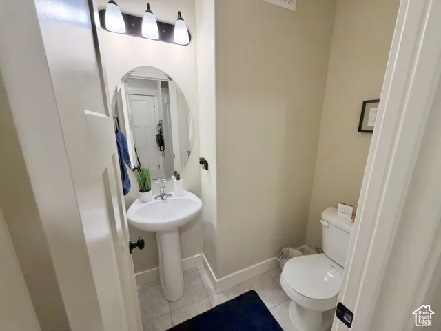 Pedestal sink with a chrome faucet, oval mirror, tile flooring, and three-light vanity fixture