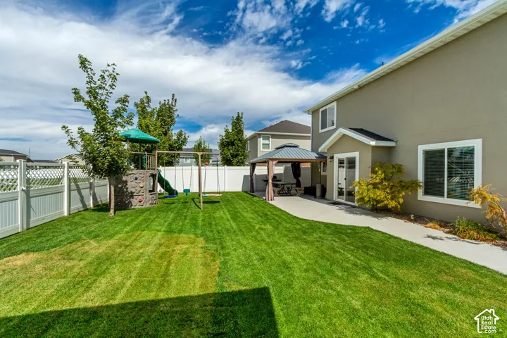 Expansive green lawn with a privacy fence, concrete patio, and a built-in gazebo structure