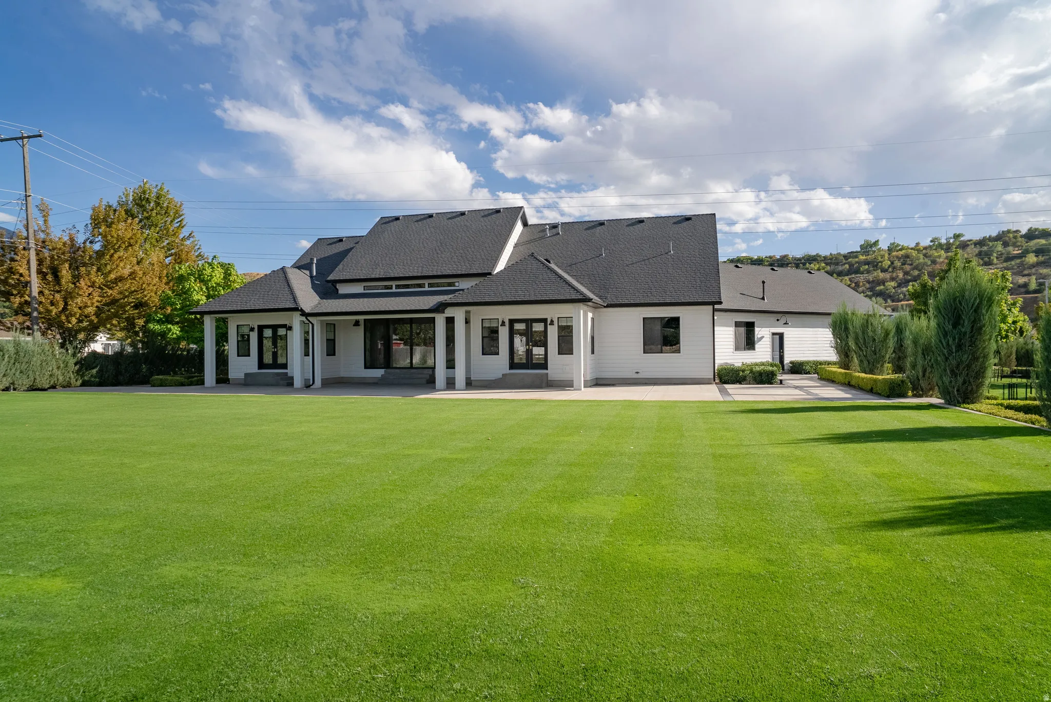 Expansive green lawn with a white exterior residence featuring a dark roof, multiple windows, and a covered patio area