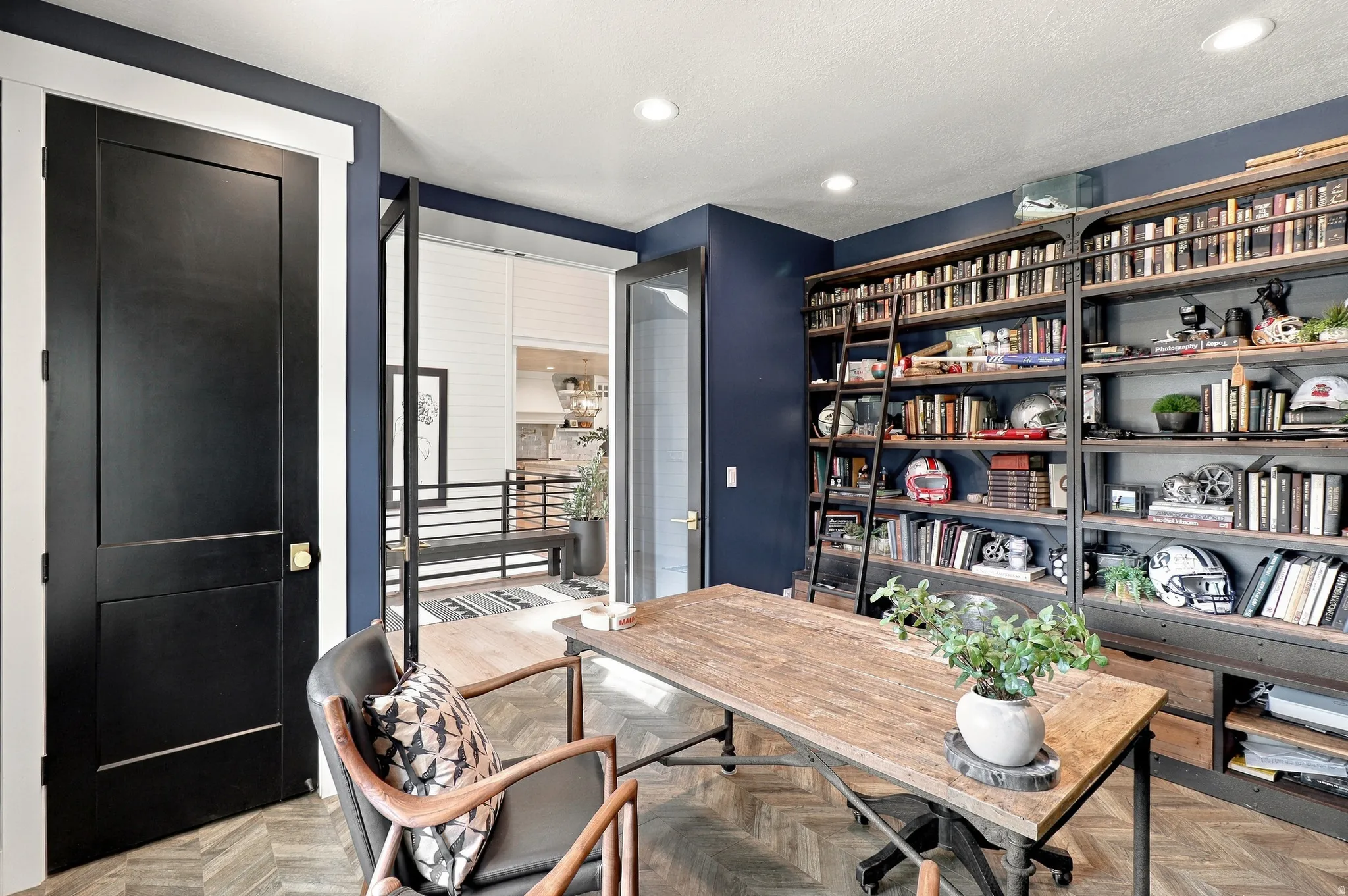 Built-in custom shelving with a rolling ladder, wood-finish herringbone flooring, dark panel doors, and recessed lighting