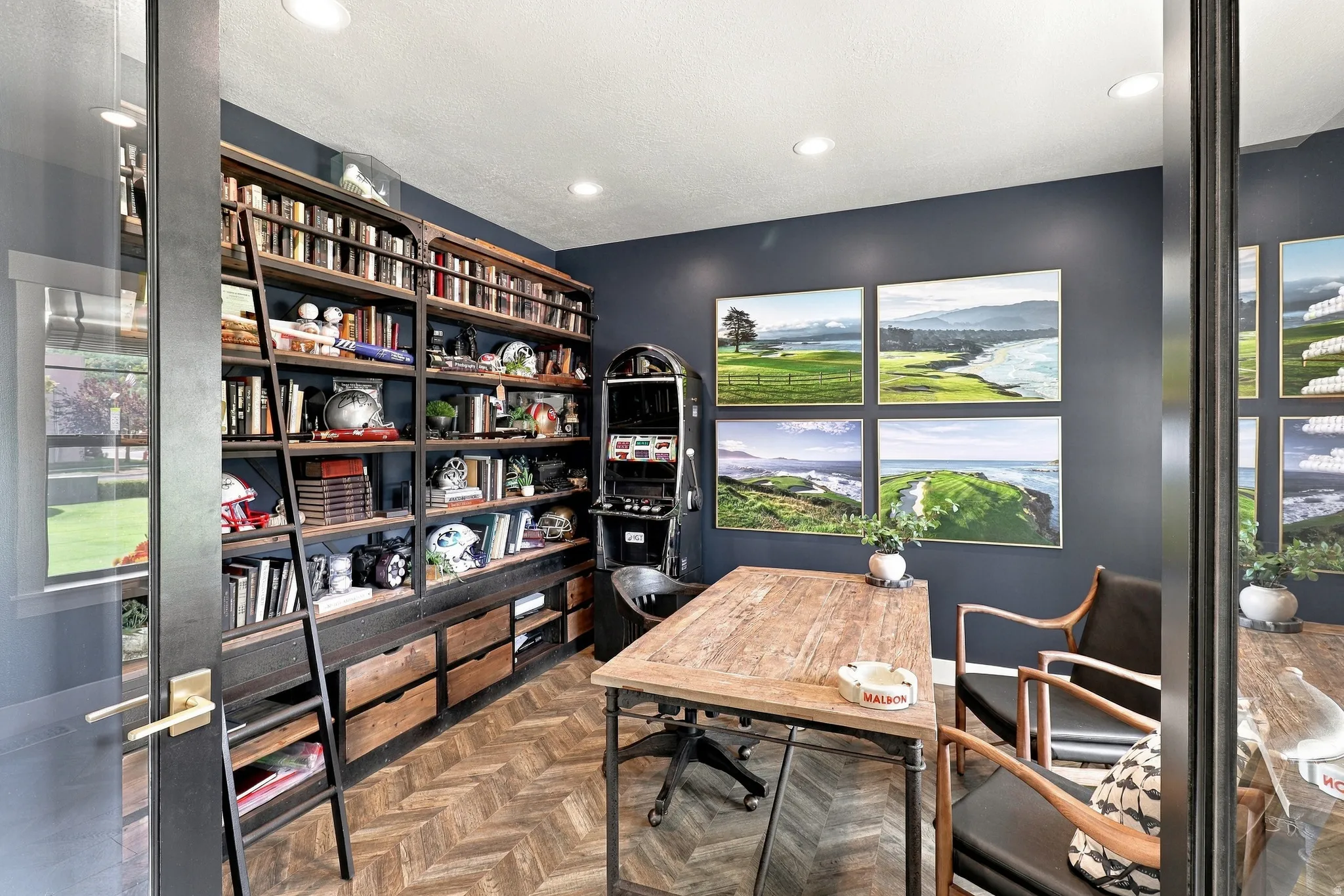 Herringbone wood-finish flooring, extensive built-in shelving with a rolling ladder, recessed ceiling lighting, and a window with exterior views