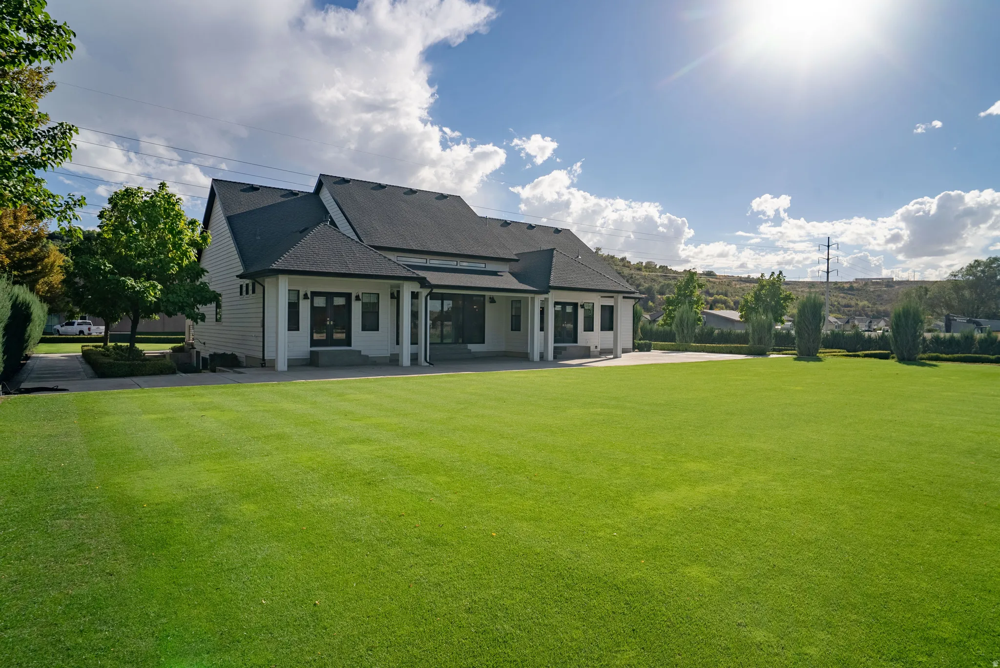 Expansive green lawn, dark-toned hip roof, light-colored siding, covered patio with white pillars, and prominent exterior lighting