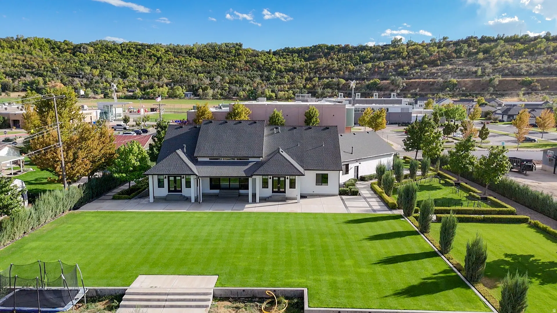 Expansive rear lawn with manicured landscaping, a paved patio, and a backdrop of natural hills