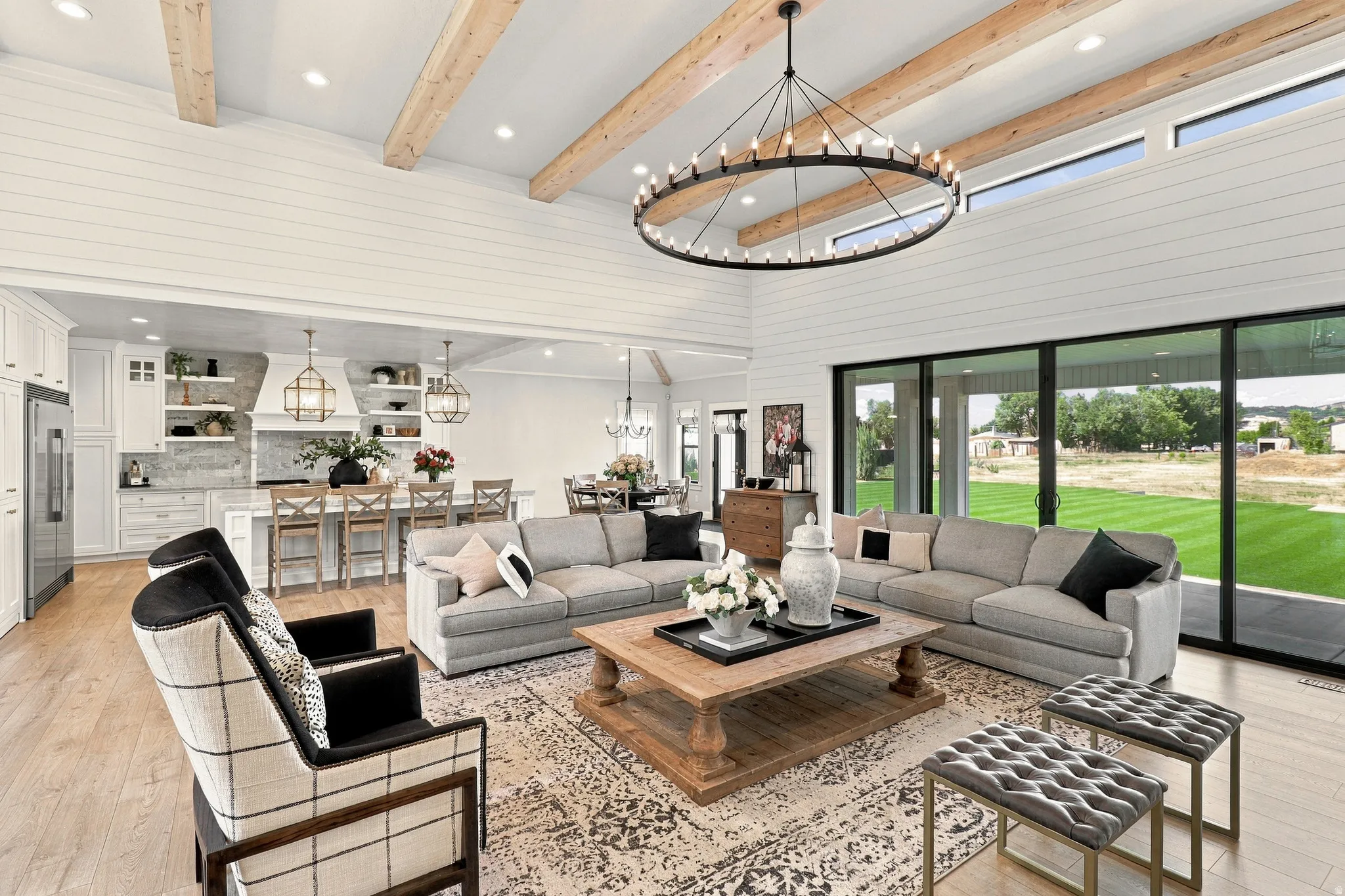 Vaulted ceiling with exposed wood beams, expansive sliding glass doors, white shiplap walls, wood-finish flooring, and a large open-concept kitchen with an island