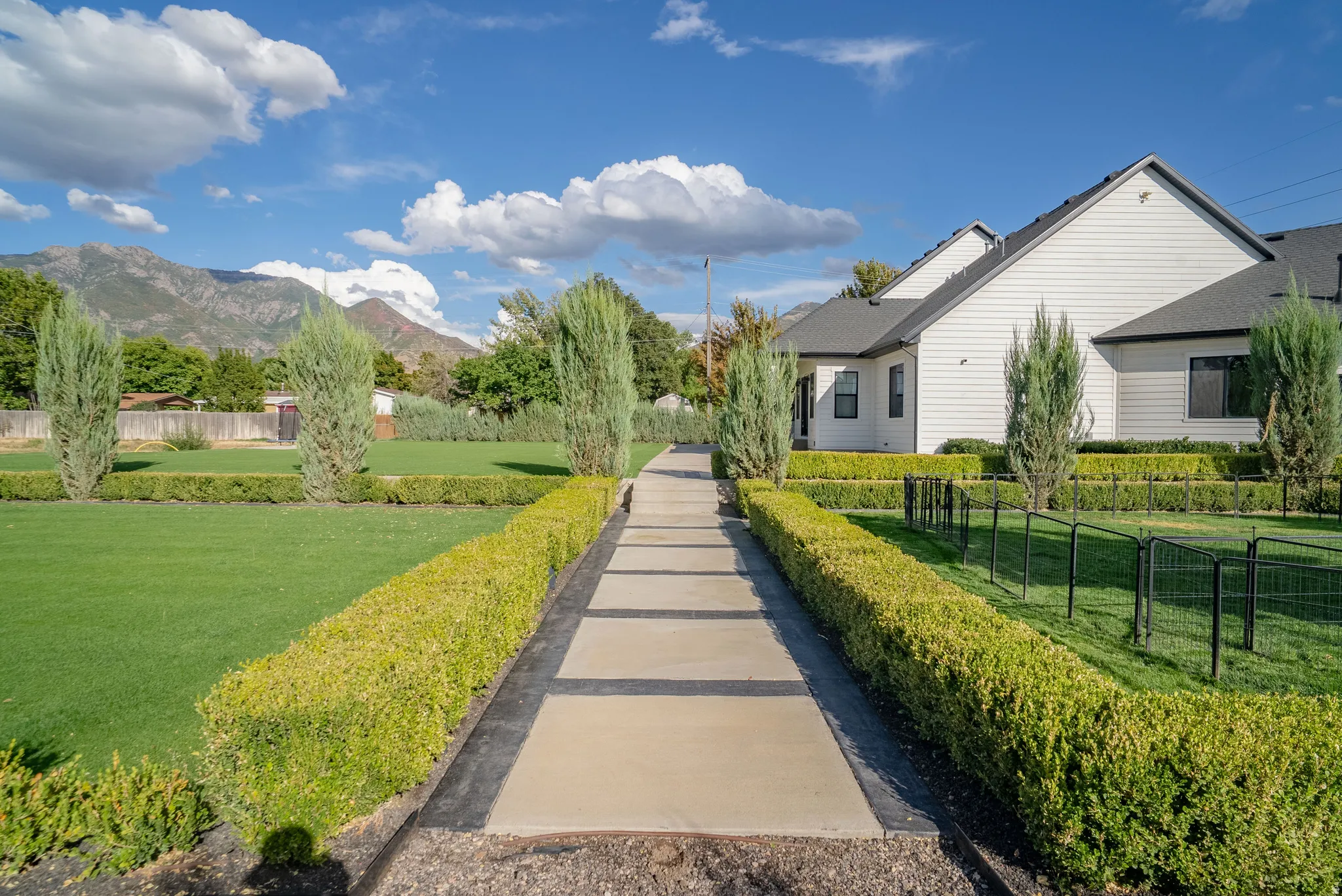 Expansive lawn featuring manicured hedges, mature evergreen trees, and a patterned walkway