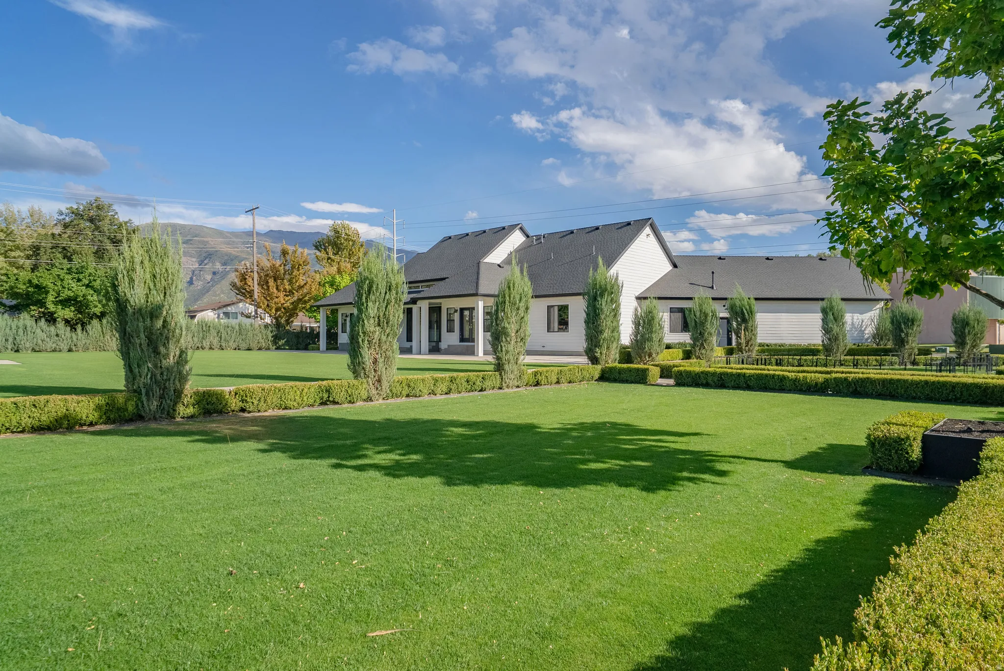 Expansive backyard featuring a manicured lawn, established privacy hedges, and mature trees