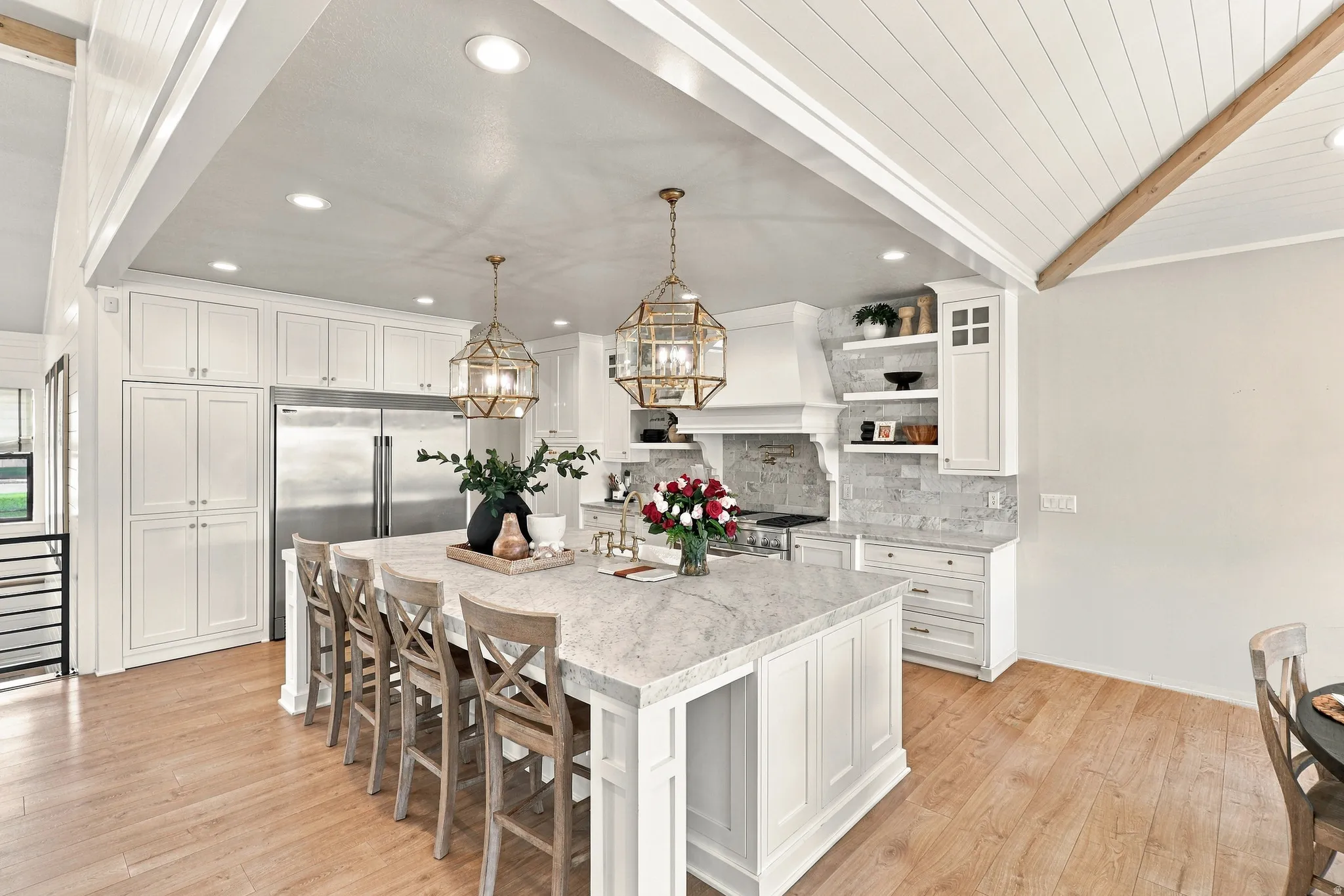 Spacious kitchen featuring an expansive central island with stone countertop, white cabinetry, wood-finish flooring, recessed lighting, and decorative pendant fixtures