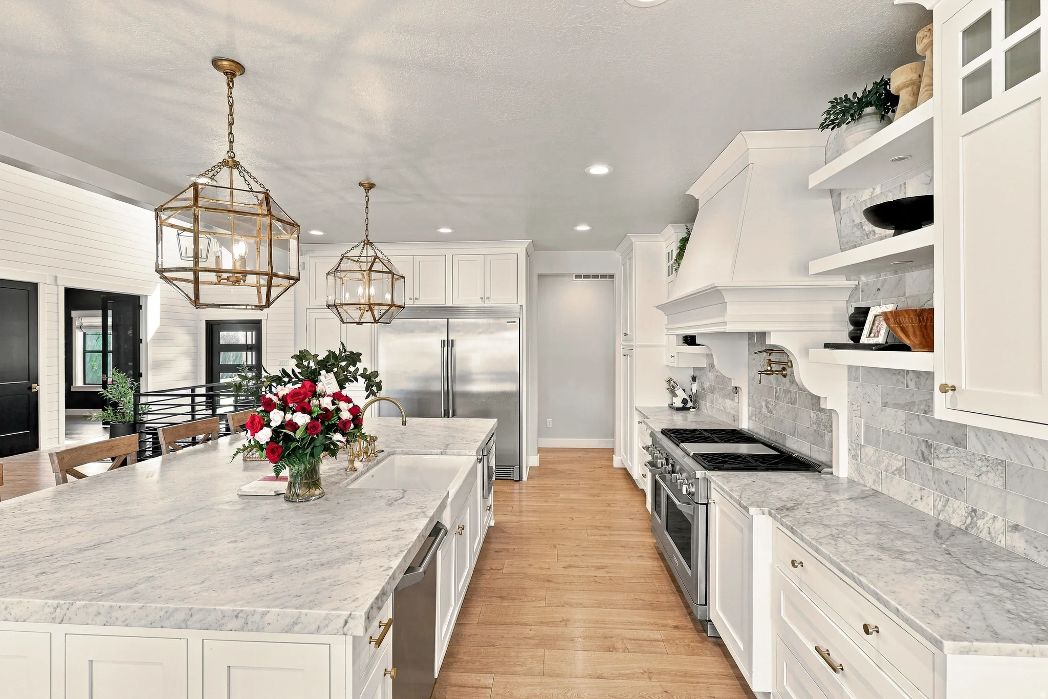 Gourmet kitchen featuring a large island with white stone countertops, white shaker cabinetry, stainless steel appliances, and wood-finish flooring