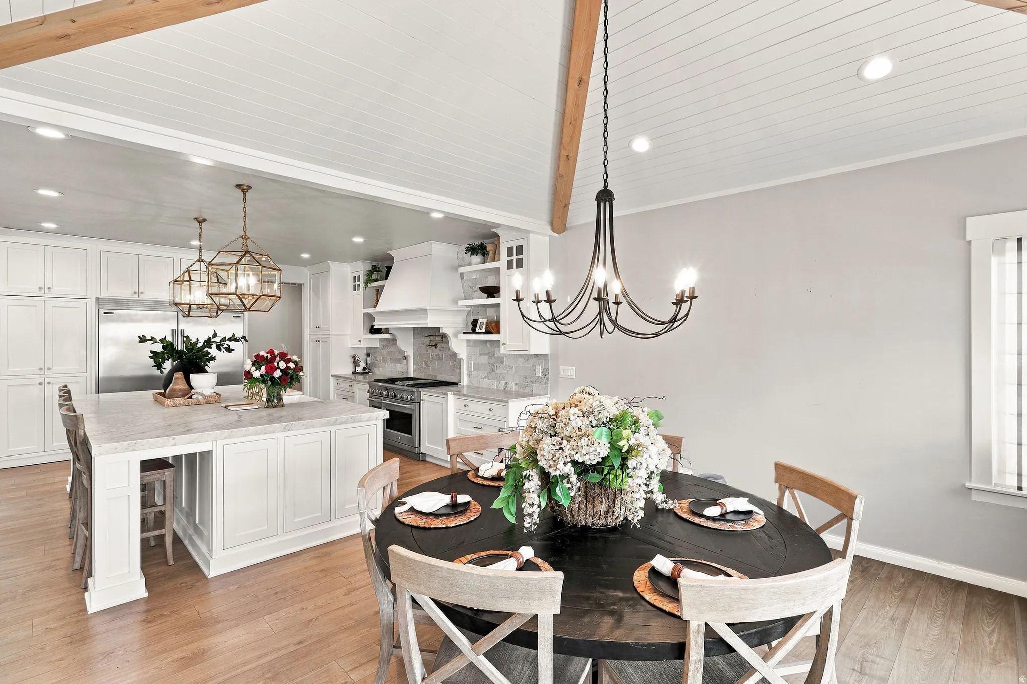 Open-concept dining area and kitchen with wood-finish flooring, exposed wood beams, and a white beadboard ceiling