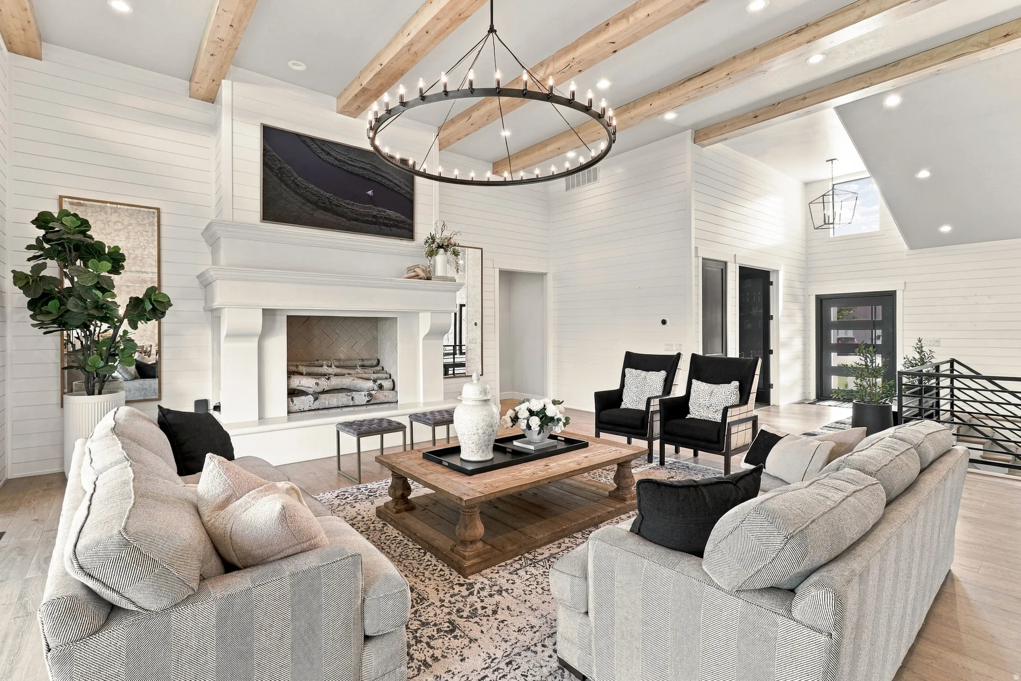 Vaulted ceiling with wood beams, shiplap walls, wood-finish flooring, a large fireplace with a substantial mantel, and a multi-pane glass entry door