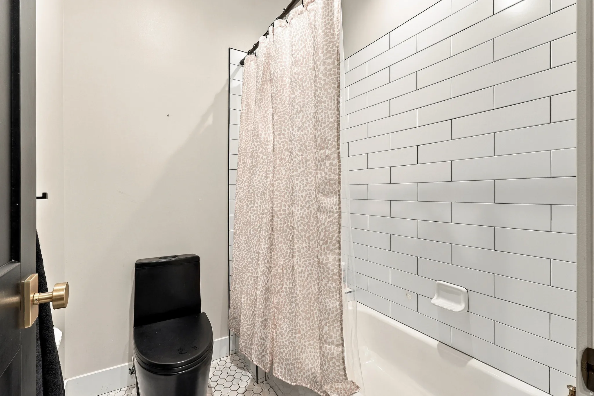White subway tile shower surround with integrated tub, black toilet, and hexagonal floor tiles