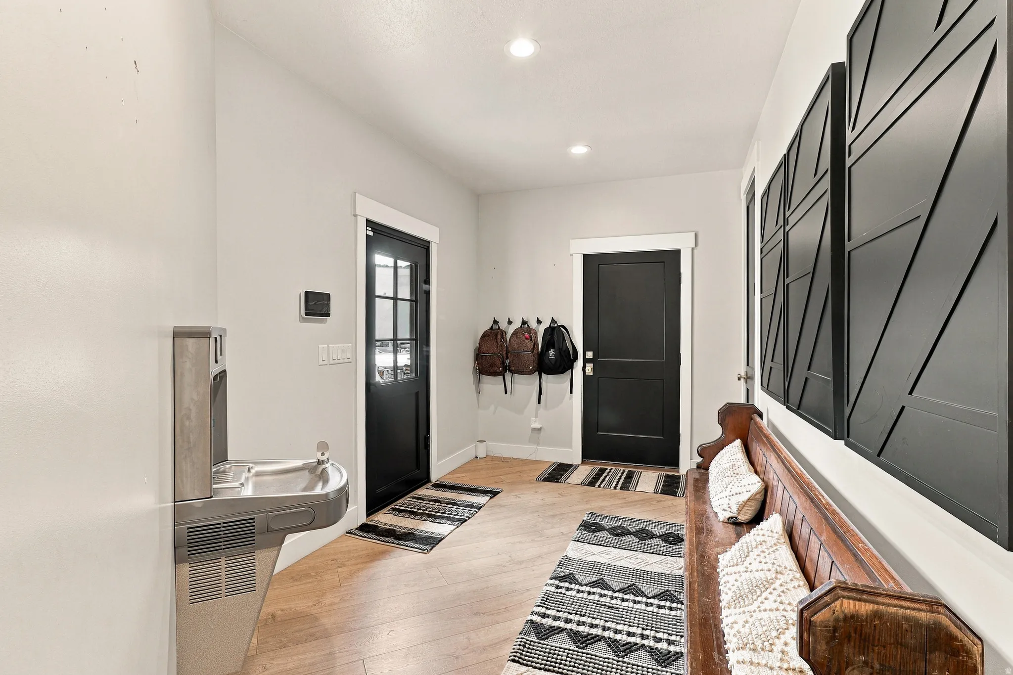 Recessed ceiling lighting illuminates the entry hall featuring wood-finish flooring, a wall-mounted water fountain, and dark doors with white trim