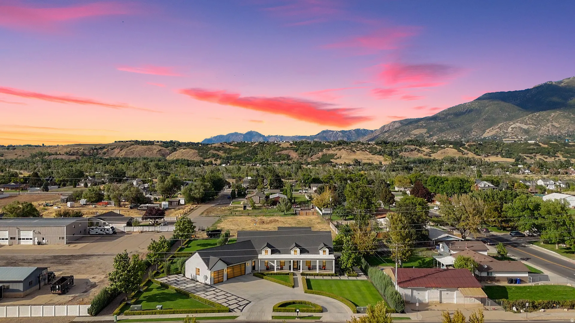 Expansive property featuring a circular paved driveway, manicured lawn, and a light-colored exterior with a dark roof