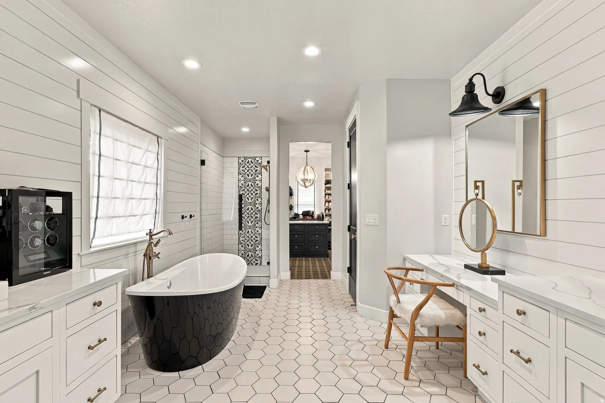 Freestanding soaking tub, white hexagon tile flooring, white shiplap wall paneling, dual vanity with white countertops, and a glass-enclosed shower with patterned tile accents