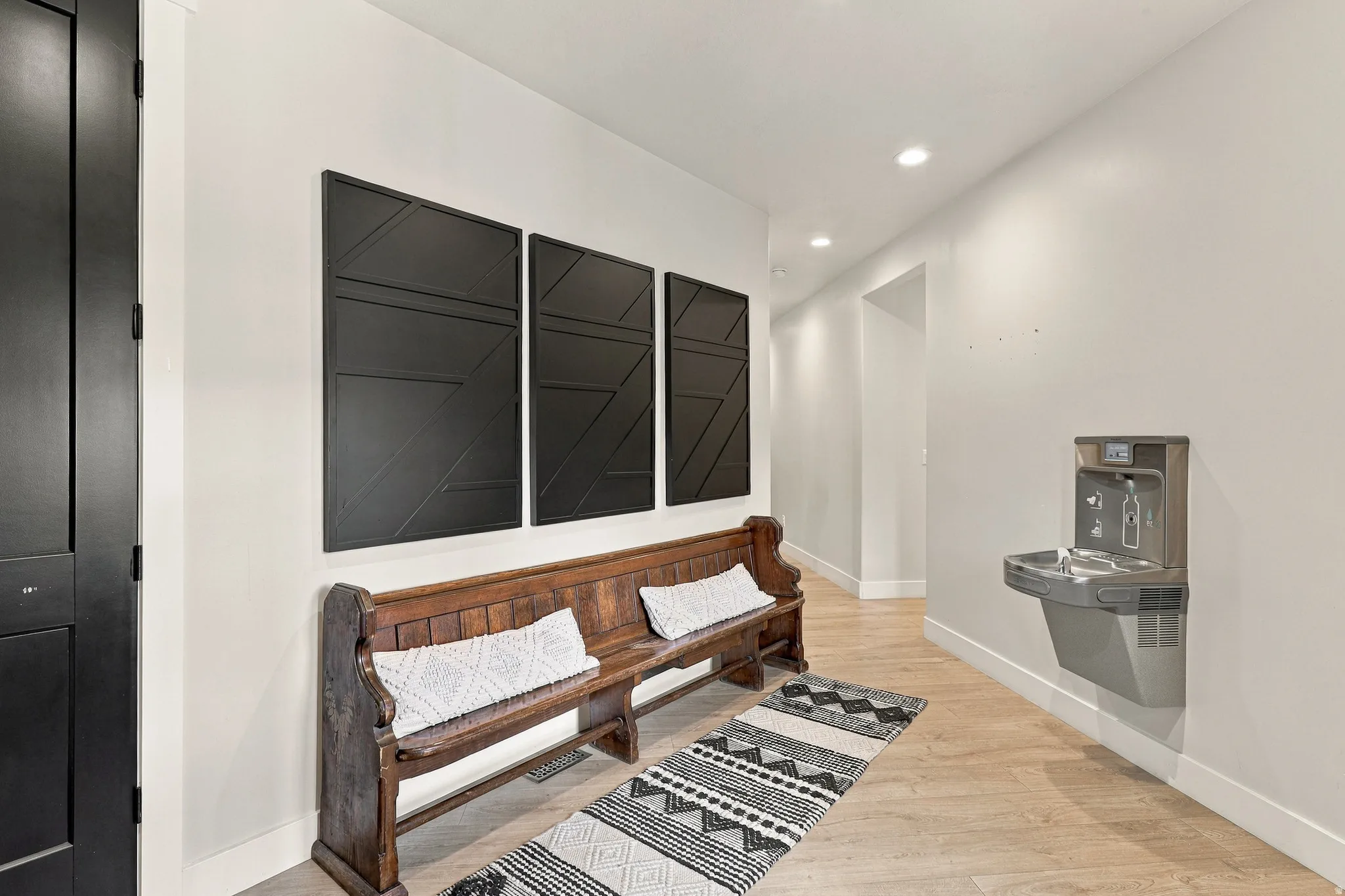 Wood-finish flooring with recessed lighting, dark interior door, and a built-in drinking fountain