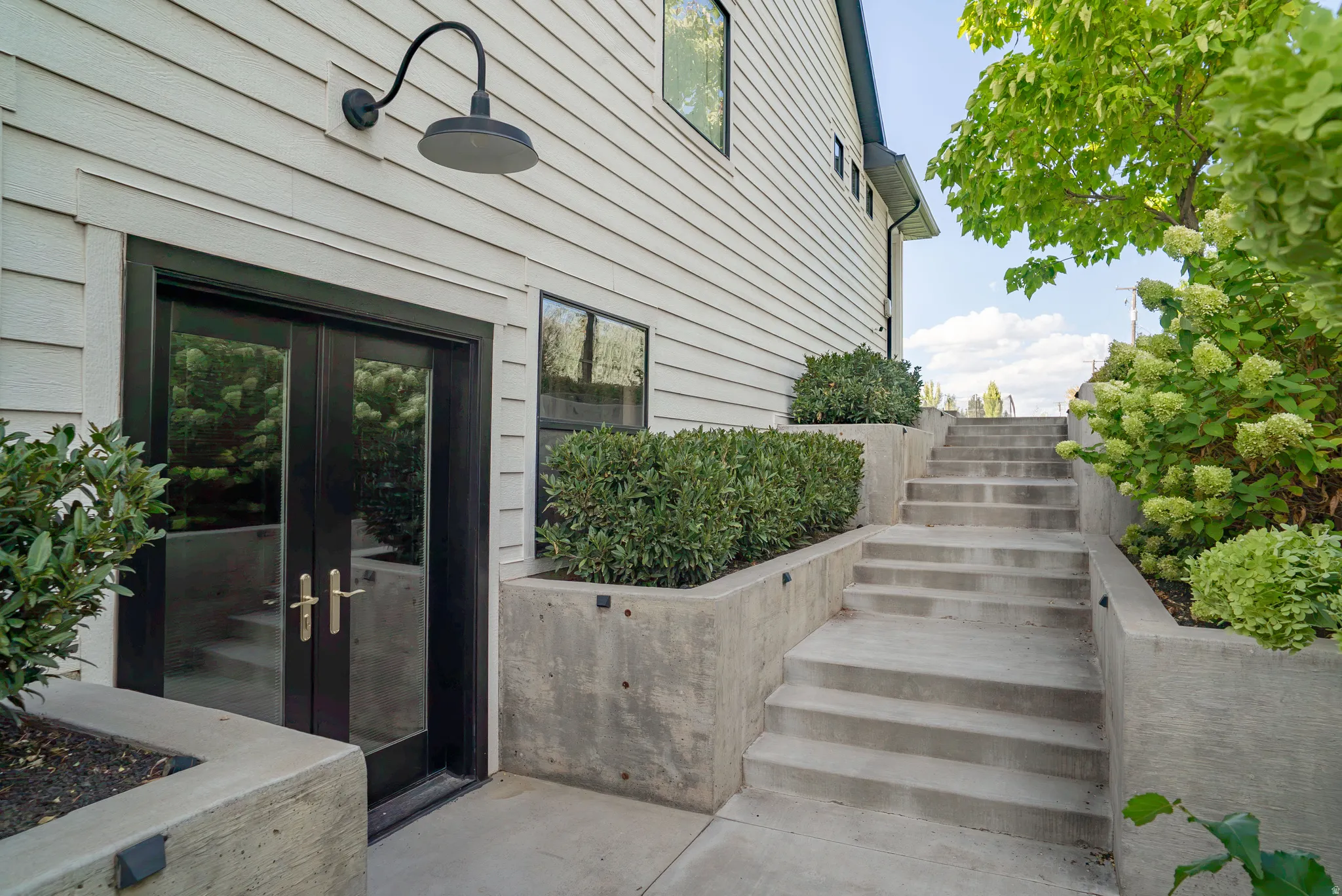 White siding exterior with black-framed French doors and a gooseneck light fixture