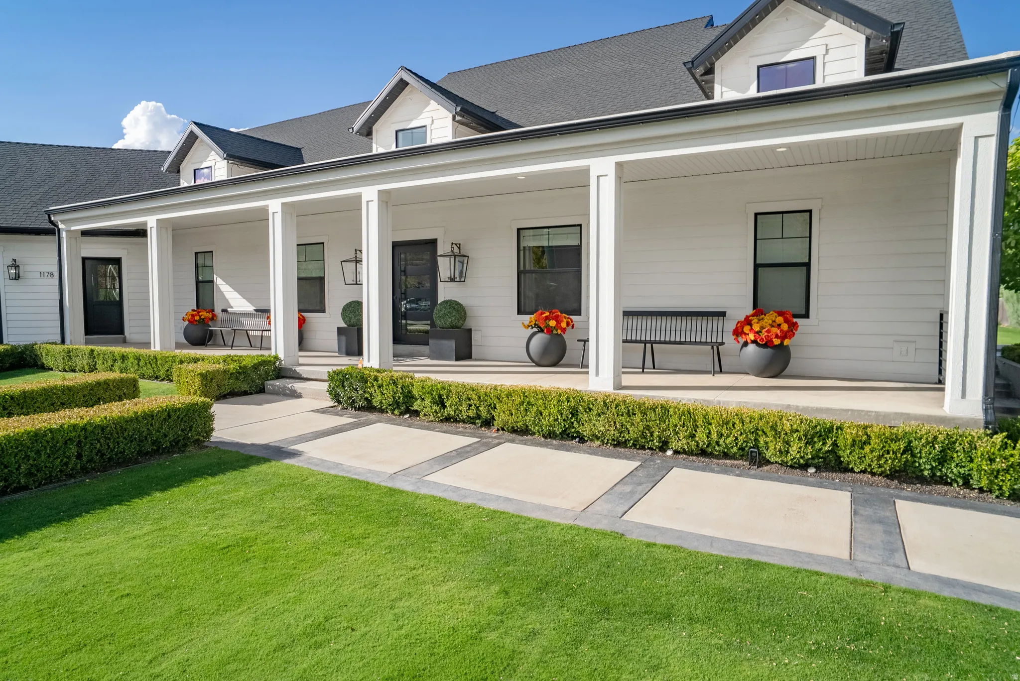 Expansive covered front porch with white columns, dark roof, and white siding