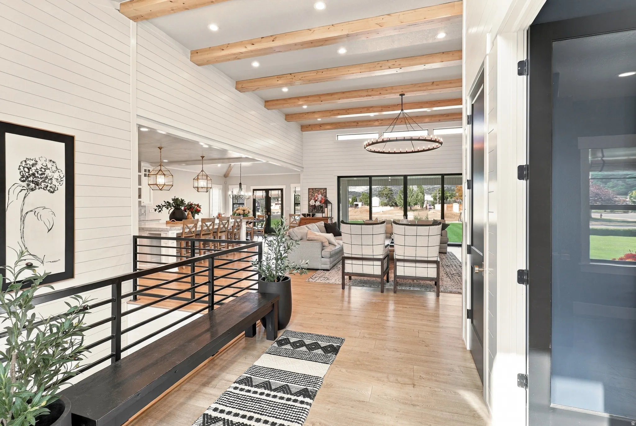 High ceilings with exposed wood beams, shiplap wall finishes, wood-finish flooring, black metal railing, and large glass paneled doors