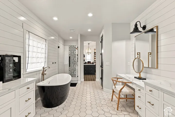 Freestanding soaking tub, white hexagon tile flooring, white shiplap wall paneling, dual vanity with white countertops, and a glass-enclosed shower with patterned tile accents