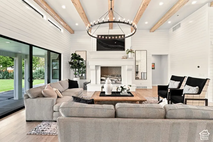 Vaulted ceiling with exposed wood beams, white shiplap walls, wood-finish flooring, white fireplace, and black-framed sliding glass doors