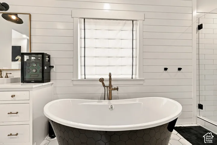 Freestanding soaking tub with a hexagon tile exterior, shiplap wall finishes, frameless glass shower enclosure, and a window with a Roman shade