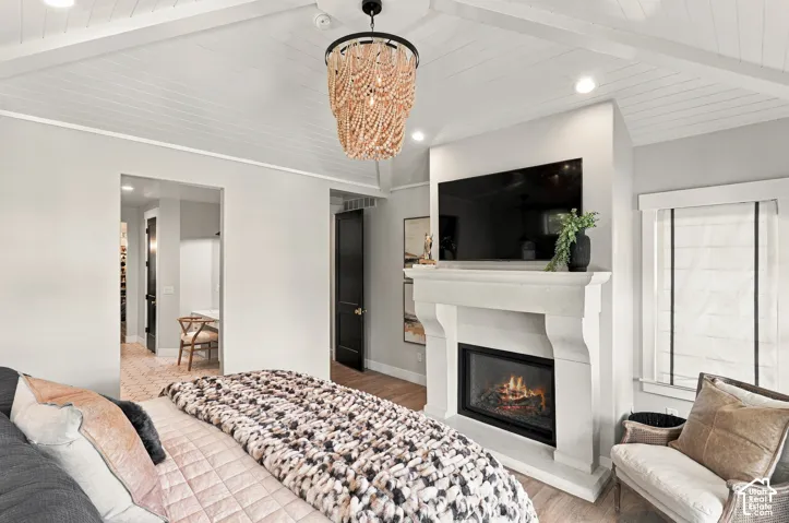 Vaulted shiplap ceiling with exposed beams, decorative chandelier, built-in fireplace with stone-finish mantel, recessed lighting, and wood-finish flooring