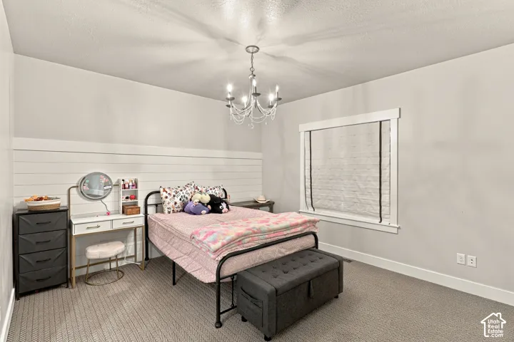 Carpeted flooring, white shiplap accent wall, chandelier lighting, and a window with white trim