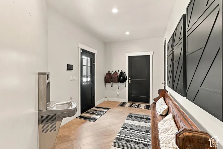 Recessed ceiling lighting illuminates the entry hall featuring wood-finish flooring, a wall-mounted water fountain, and dark doors with white trim