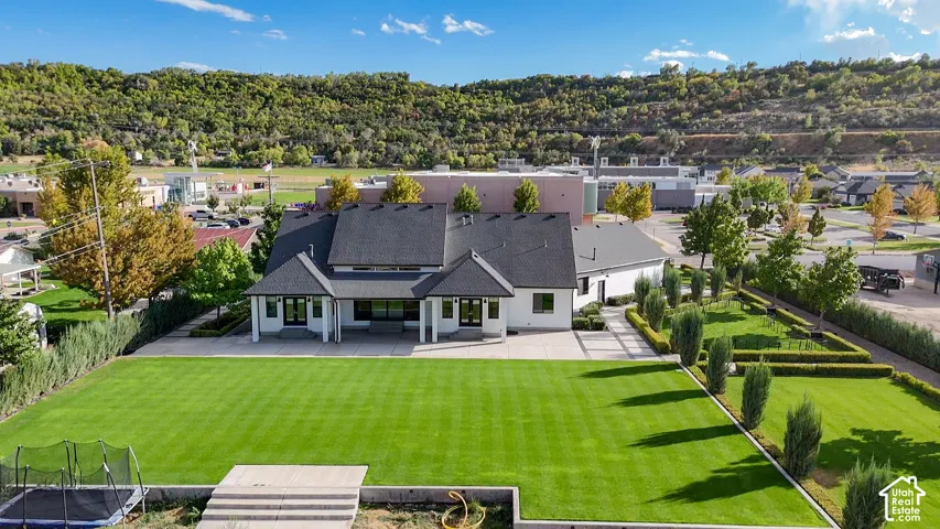 Expansive rear lawn with manicured landscaping, a paved patio, and a backdrop of natural hills