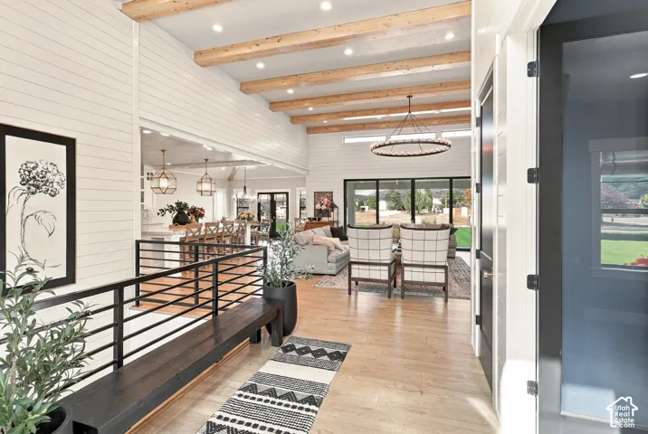 High ceilings with exposed wood beams, shiplap wall finishes, wood-finish flooring, black metal railing, and large glass paneled doors