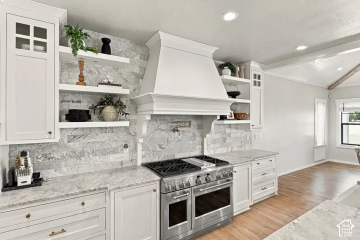 Stainless steel range, white shaker cabinetry, stone countertops, stone tile backsplash, and recessed lighting