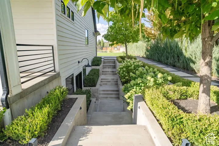 Exterior featuring white horizontal siding, black horizontal railing, concrete steps, built-in planters with shrubs, and mature trees